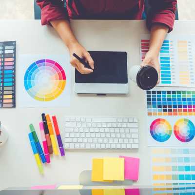 Persona usando una tableta gráfica rodeada de muestras de color y herramientas de diseño.